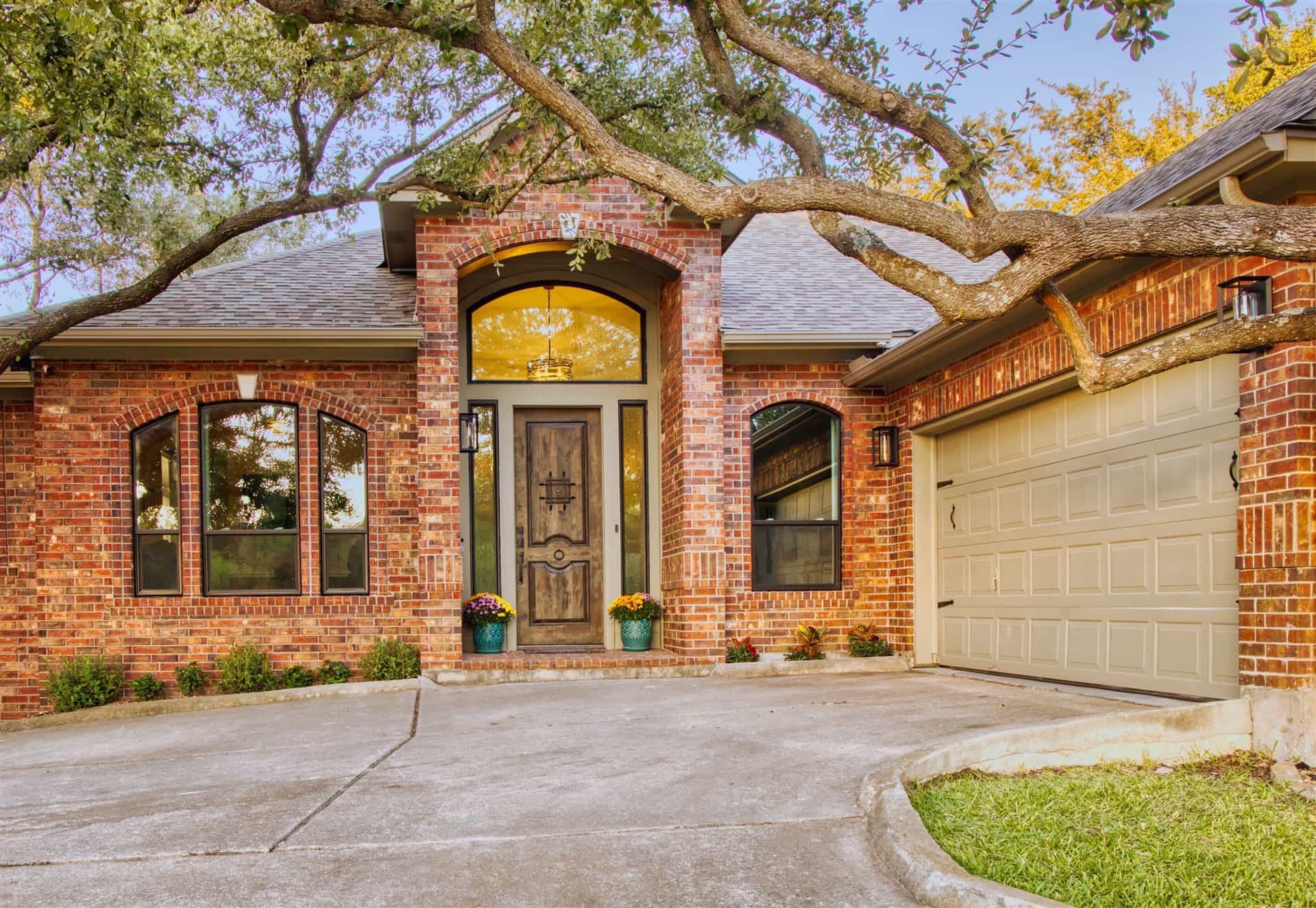 Beautiful brick home with new arched windows and oak tree canopy by Glacier Home Exteriors in Central Texas
